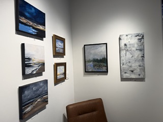 Gallery wall featuring a collection of abstract landscape paintings in various sizes and frames, with a brown leather chair in the foreground.