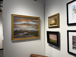 An art gallery wall displaying four framed paintings, including a large landscape painting with a sunset, and three smaller artworks in varying frames.