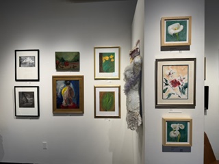 An art gallery wall displaying a variety of framed artworks, including paintings and photographs, featuring floral and abstract themes.