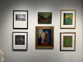 Gallery wall featuring a collection of framed artworks, including landscapes, floral paintings, and abstract pieces, arranged in two vertical columns.
