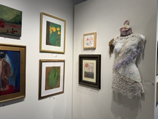 An art display featuring various framed paintings on a wall and a decorative dress form adorned with intricate fabric and lace.