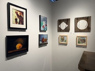 An art gallery wall displaying a variety of framed paintings, including abstract and still life artworks, arranged in a visually appealing manner.